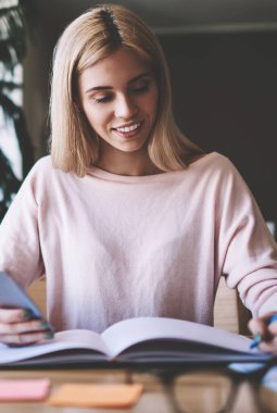 Bir sonraki toplantı için ders kitabında mobil organizatörden notları işaretleme bilgi olayların başarılı kadın organizatörü, mutlu hipster kız internet tarama için hücresel kullanarak üniversite testine hazırlanıyor