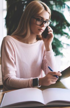 Ciddi kadın tasarımcı üniversite gazetesi için yeni tamamlanan illüstrasyon kroki tartışmak için meslektaşım çağrıda, göz gözlük içinde konsantre hipster kız önemli Smartphone konuşma yapma