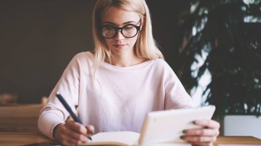 Akıllı kadın yazar, bin yıllık insanlar hakkında makale hakkında bilgi düşünme, gözlükler Genç beyaz kadın eğitim için ders kitabı ile masada otururken çalışma için zaman harcamak