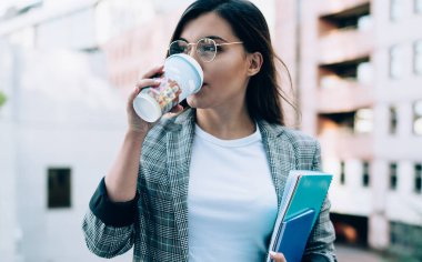 Eğitimle ilgili ders kitabı olan çekici bir kız öğrenci molada lezzetli kafein içeceği içiyor, resmi giyinmiş Türk kadın kahveyi seviyor ve düşünüyor.