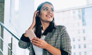 Cep telefonu elinde başarılı bir kadın girişimci kent ortamını bekleyen bir arkadaşı beklerken yüzünü çevirmiş gülümsüyor, olumlu Türk iş kadını modern teknolojiyle boş zamanların tadını çıkarıyor