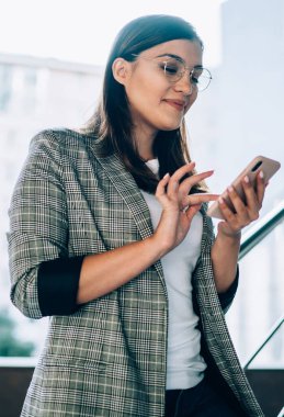 Gülümseyen genç bir kadın akıllı telefondan mesaj yolluyor şehir ortamında duruyor, olumlu modacı hippi kız sosyal ağda internet bağlantısı olan cep telefonu kullanıyor.