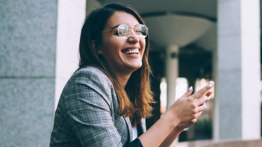 Modern cep telefonlu neşeli yeniyetme kız portresi şehir ortamında boş zamanlarında gülüyor, mutlu Türk milenyum kadını cep telefonundan içerik mesajı alıyor.