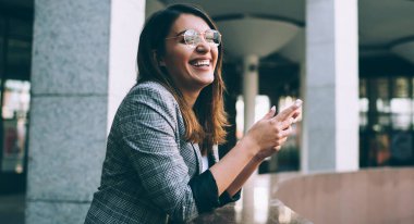 Modern cep telefonlu neşeli yeniyetme kız portresi şehir ortamında boş zamanlarında gülüyor, mutlu Türk milenyum kadını cep telefonundan içerik mesajı alıyor.