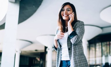 Akıllı telefon zımbırtısıyla yapılan uluslararası arama sırasında alınan bilgilerle gülen neşeli bayan girişimcinin yarım boy portresi, arkadaşıyla cep telefonu konuşması yapan pozitif kadın.