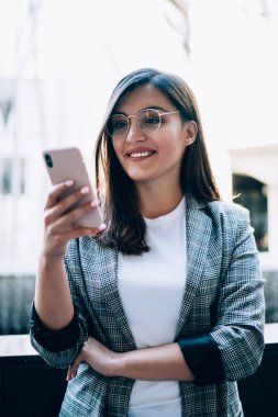Genç gülümseyen hippi kız modern teknolojiyi şehir ortamında kullandığı için eğleniyor, mutlu kadın akıllı telefon cihazında online oyun bildirimi için kontrol ediyor.