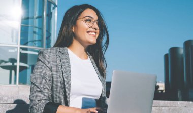 Modern bilgisayar cihazıyla şehir ortamında otururken mutlu bir metin yazarı gözlerini kaçırıyor ve gülümsüyor. Gözlüklü pozitif hippi kız dışarıda öğrenim görüp kendini iyi hissediyor.
