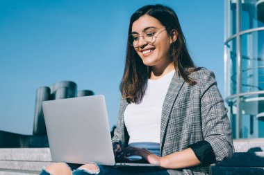 Şirin tebessümlü, klavyeli güzel bir kız öğrenci üniversitedeki derslerden sonra dinlenirken dışarıda merdivenlerde otururken dizüstü bilgisayarında çalışan neşeli mutlu bir kadın.