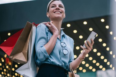 Web mağazası servisinden geri bildirim bekleyen mutlu kadın müşteri, elinde akıllı telefon cihazıyla heyecanlı kadın alışverişi kolikler, sosyal ağdaki komik yayınlardan gülüyor.
