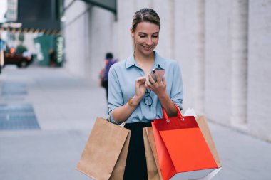 Mutlu hipster kızı bilgi aramak için cep telefonunu kullanıyor, web sitesinden olumlu haberler okuyor, takipçilerle her gün akıllı telefon uygulaması üzerinden iletişim kurmaktan keyif alan gülümsüyor.