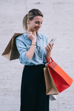 Neşeli bayan alışverişçi teslimat için telefon görüşmesi yapıyor, genç gülümseyen bir kadın kağıt torba tutuyor ve promosyon arka planında fotokopi alanı ile duruyor.