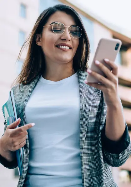 Görüş düzeltmesi için gözlüklü çekici bir kadın şehir ortamında iş arkadaşından gelen e-postayı kontrol ediyor, resmi ceketli pozitif bayan yönetici içerik profili hakkında komik haberler okuyor.