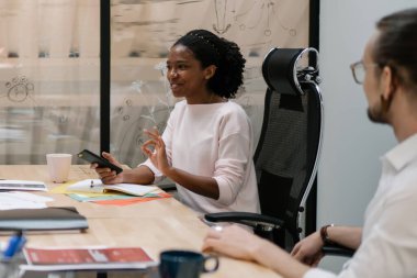 Modern ofiste birlikte çalışan başarılı erkek ve kadın girişimciler, iş birliği yapan ve kapalı alanda iletişim kuran pozitif çok kültürlü ortaklar.