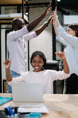Resmi giyinmiş çok kültürlü girişimciler zaferi kutlarken modern ofiste beyin fırtınası yapıyorlar. Çok mutlu çalışanlar dizüstü bilgisayardaki iş projesini başarıyla tamamladı.