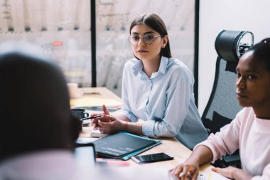 Masaüstünde oturan çok kültürlü erkek ve kadın tüccarlar finans direktöründen yeni iş stratejileri dinliyorlar. Konferans için zaman harcayan ciddi bir grup profesyonel iş arkadaşının arka planı.