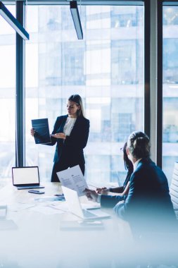 Resmi takım elbise giymiş kendine güvenen bir kadın yönetmen, reklam metni veya finansal web sitesi için boş ekran alanı olan dizüstü bilgisayarlı üretken stratejinin sunumunu yapıyor.