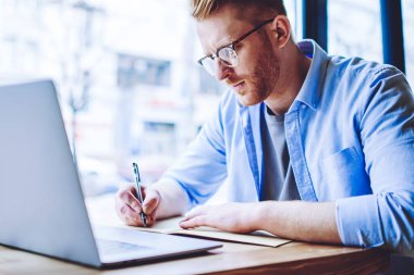 Kampüs kafeteryasında e öğrenme sırasında bilgi ders kitabında ciddi erkek öğrenci yazma Okulu testi, görme düzeltmesi için gözlerde genç hipster adam Not defteri 'nde ödev yapıyor kapalı okuyan