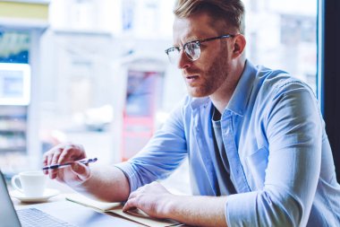 Gözlükler içinde konsantre erkek öğrenci dizüstü bilgisayar üzerinde dosya ders çalışması hakkında veri bilgilerini kontrol ve eğitim için ders kitabında planı analiz, teknoloji ve iletişim kavramı