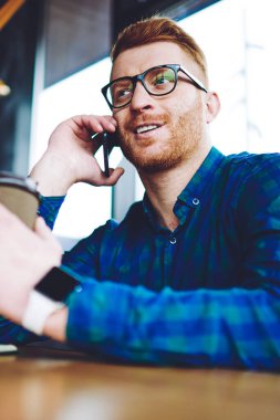 Tanıtım alanında kahve molası sırasında olumlu akıllı telefon konuşma zevk gözlük Mutlu gülümseyen hipster adam, başarılı erkek öğrenci boş zamanlarında iletişim kurmak için arkadaşa çağrı