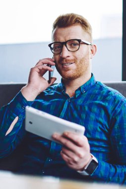 Elinde dokunmatik yüzey tutan arkadaşı ile olumlu akıllı telefon konuşma sırasında kameraya bakan ve wifi bağlantısı, teknoloji ve nesil kavramı bekleyen mutlu gülümseyen adam Portresi