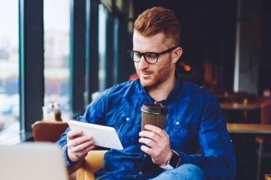 Dizüstü bilgisayar üzerinde çalışma mola sırasında modern dokunmatik yüzey üzerinden online video izlerken gözlük erkek freelancer, dijital tablet ve netbook üzerinden dosya paylaşımı sırasında kahve molası zevk bin yıllık adam