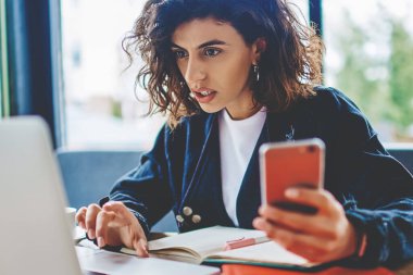Modern uzayda dizüstü bilgisayarda kablosuz internet kullanan heyecanlı, kısa saçlı genç bir kadın dijital akıllı telefonu elinde tutarken, web sitesinde şok videosu izliyor.
