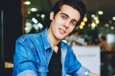 20 yaşında kot ceket giymiş yakışıklı bir gencin portresi. Kameraya bakıyor. Not defterine bilgi yazıyor.