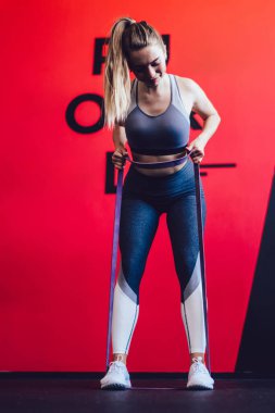 Spor salonunda kilo vermenin tadını çıkaran vücut geliştirici spor yaparken elastik kauçuk kullanan beyaz bir bayan sporcu.