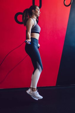 Modern pilates stüdyosunda idman sırasında ip atlayan genç bir kadın zayıflama için fiziksel antrenmana konsantre olmuş, spor kıyafetleri içinde atlayan çekici, aktif hippi kız.