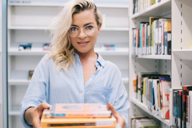 Vizyon düzeltmesi için moda gözlüklü genç kadın kütüphanecinin yarım boy portresi eğitim için kitap tutuyor ve bunları okuma, bilgi ve eğitim kavramı için sunuyor.