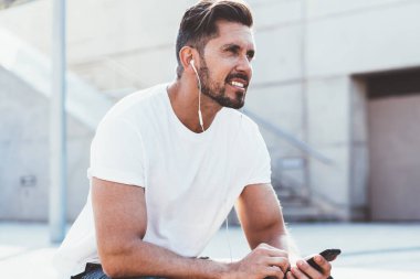 Spor kıyafetleri giymiş yakışıklı aktif bir adam. Etiket için boş ekranı var. Şehir ortamında koşuyor, kulaklık takan erkek koşucu sağlıklı bir yaşam tarzı için vücudunu formda tutuyor.