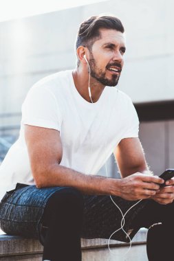 Yakışıklı bir erkek koşucu şık giyinmiş. Gözünü kaçırıyor. Cep telefonuyla 4G internete bağlanan ses tavsiyelerini dinliyor.