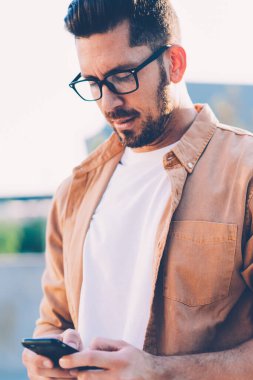 Gözlüklü yakışıklı beyaz adam akıllı telefon uygulaması aracılığıyla internet sitelerine, teknoloji ve iletişim kavramına bağlı olarak 4G kablosuz olarak mesaj yazarak göz koruması sağlıyor.