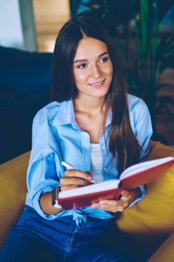 Pozitif hippi kız elinde eğitim kitabı tutuyor ve kapalı alanda kendini iyi hissediyor başarılı bir kadın üniversitede iç dekorasyonla oturuyor ve organizasyon planlamak için zaman harcıyor.