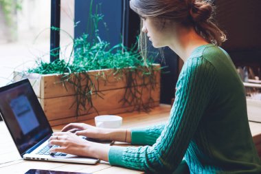 Modern laptop cihazıyla kafeterya masasında otururken ve iletişim için uygulama uygulaması aracılığıyla program kodu yazarken uzaktan çalışan genç bir kadın serbest yazar.