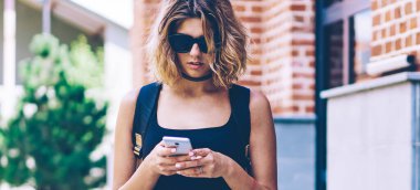 Şehir Caddesi üzerinde taksi beklerken güneş gözlüğü arama numarası cep telefonu genç hipster kız, akıllı telefon aracında navigasyon uygulaması ile çekici kadın turist izleme GPS