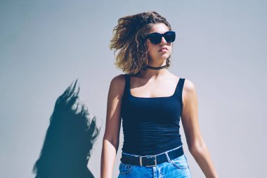 Güneşli yaz gününde duvarın yanında dikilen günlük kıyafetli genç hippi kız, şehirde yürüdükten sonra şehir merkezinde dinlenen modaya uygun kot giysili çekici beyaz kadın gezgin.