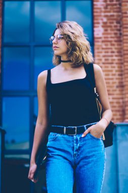 El klasörü ile Tanıtım alanında ayakta şık sırt çantası ile çekici kadın öğrenci, güneşli bir gün boyunca kentsel ortamda rahat bir görünüm bekleyen arkadaş giyinmiş güzel hipster kız