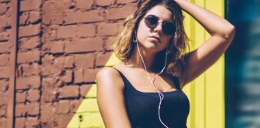 Cep telefonu kulaklıkları ve medya uygulaması ile dinleme müzik parçaları sırasında reklam alanında dinlenmek trendy güneş koruyucu kız, Genç kadın motivasyon ses kitabı zevk