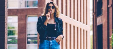 Güven kadın gezgin reklam alanında Chupa Chups ile poz tam uzunlukta portre, diğer şehirde tatiller sırasında kamera bakarak güneş gözlüğü çekici beyaz hipster kız