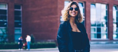 El klasörü ile üniversite kampüsü etrafında yürüyen neşeli kadın öğrenci yarım uzunlukta portre, trendy kot poz ve reklam alanında kamera bakarak mutlu gülümseyen hipster kız