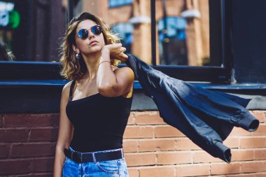 Güneş gözlüklü genç bayan üniversite öğrencisi üniversitede caddelerde yürümekten zevk alıyor. Elinde klasörle şehirde gezen modaya uygun ceketli, kendine güvenen beyaz hippi kız.