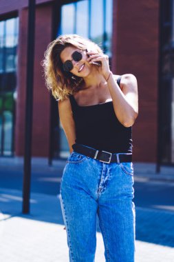 Güneş gözlüklü pozitif hipster kızın yarım boy portresi gülümseyen ve kameraya bakarken mobil uygulama üzerinden arkadaşınla uluslararası sohbet etmek için 4G gezinti bağlantısı kullanıyor.