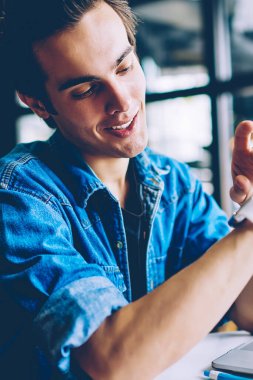 Pozitif erkek öğrenci modern bilgisayar ile kafeterya masada otururken elektronik kol saati üzerinde zaman kontrol, bin yıllık hipster adam giyilebilir akıllı saat üzerinde bildirim okuma gülümseyen