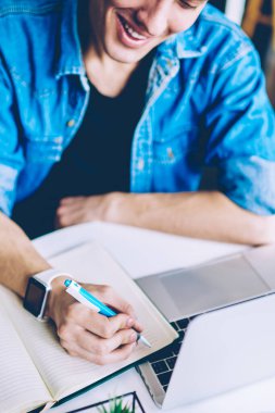 Kahve dükkanında ders kitabı öğrenme ilginç tezler yazma neşeli erkek öğrenci yakın, mutlu gülümseyen serbest, bin yıllık adam modern dizüstü bilgisayar ile oturan ve iş planlama için notlar yapma