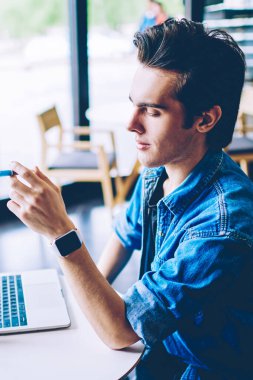 Ciddi erkek öğrenci dizüstü bilgisayar ile sehpa otururken ilginç bilgileri ezberlemek çalışırken programlama hakkında önemli web semineri izlerken, bin yıllık adam serbest uzaktan çalışmak