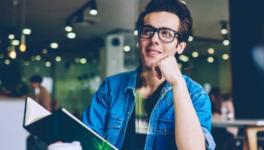 Kahve dükkanında serbest zaman diliminde edebiyat En çok satan tutarken uzak bakarak göz koruması sağlamak için gözlük pozitif hipster adam, mutlu erkek öğrenci eğitim zevk