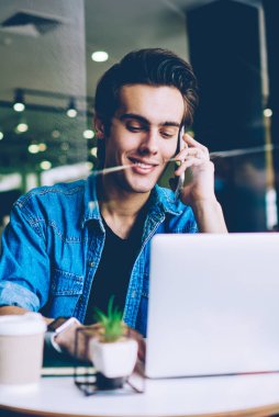 Gülümseyen erkek öğrenci dizüstü bilgisayar üzerinden şakalar ile komik web siteleri ararken olumlu telefon görüşmesi yaparken, mutlu adam cep telefonu üzerinden arama ve modern netbook e-posta yazarak