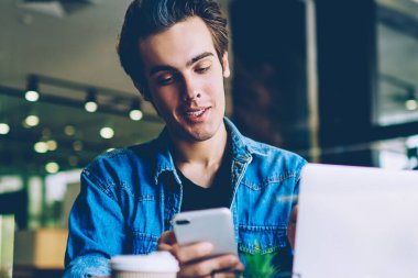 Mutlu bin yıllık hipster adam iletişim için mobil uygulama kullanarak arkadaşlarınızla mesajlaşma, arama için iletişim numarası ararken kafeteryanetbook ile oturan başarılı erkek öğrenci