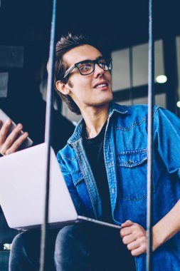 Kampüs merdivenlerinde arkadaş beklerken iletişim için dijital teknolojileri kullanarak rahat bir görünüm giymiş Neşeli erkek öğrenci, pozitif bin yıllık hipster adam 20s elinde akıllı telefon tutarak